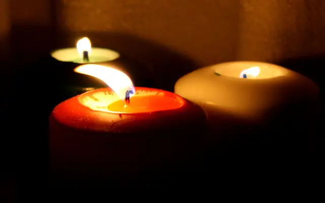 Three lit pillar candles glowing warmly in a dark room